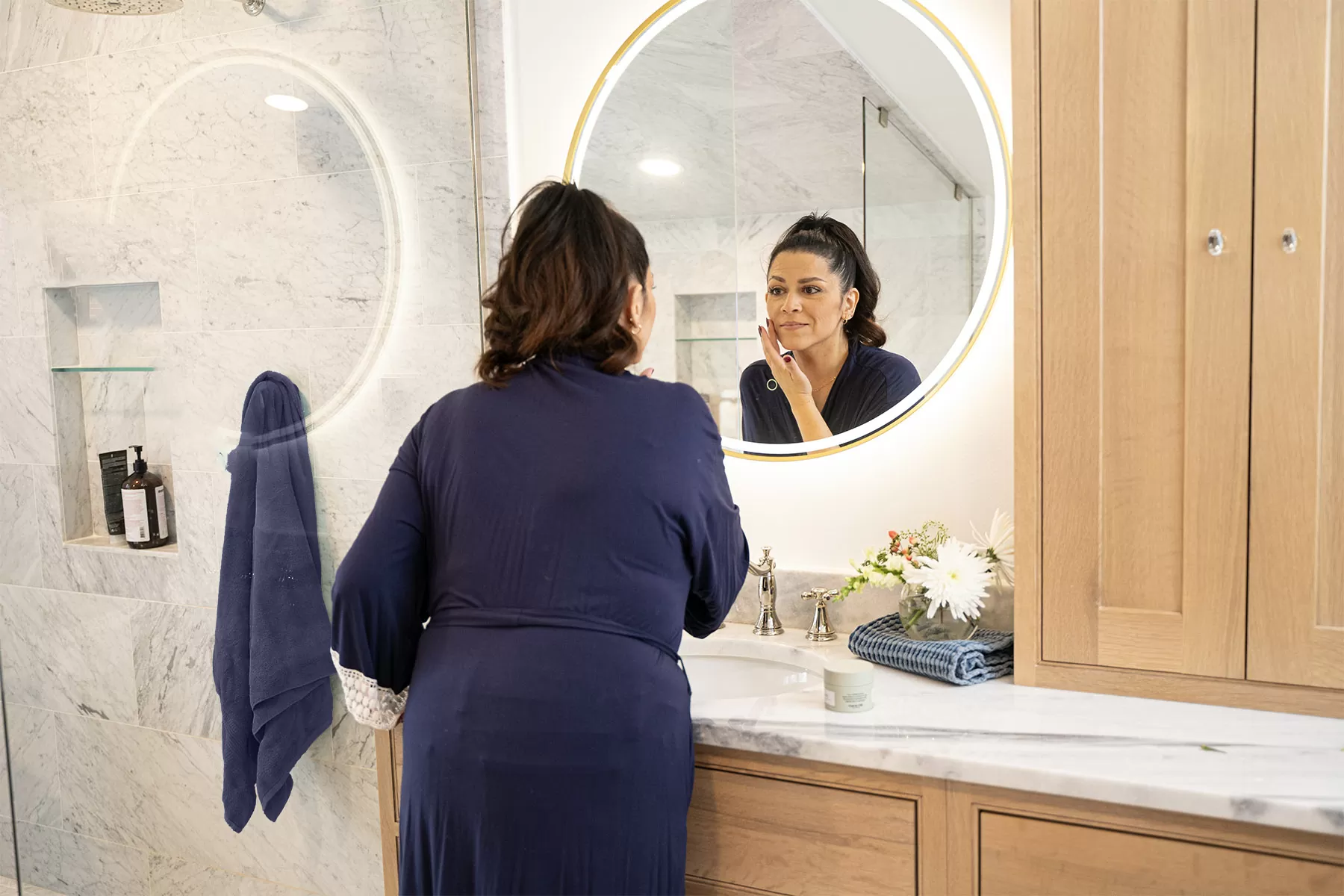 woman standing in front of mirror applying skincare
